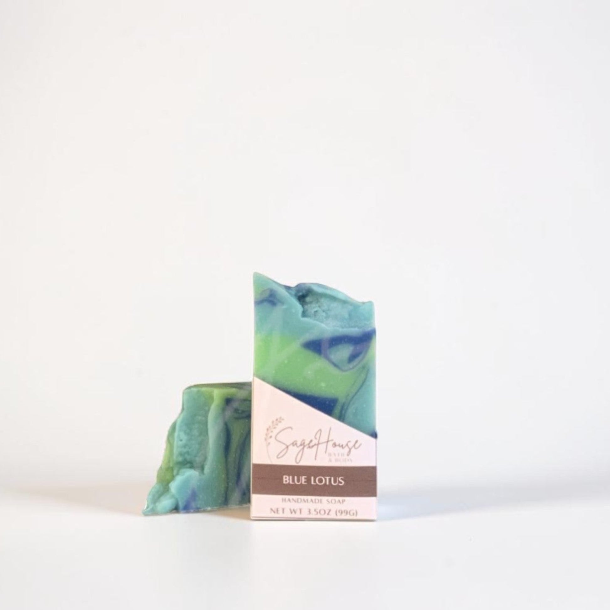 A bar of soap with a blue and green marbled pattern, standing upright next to its paper packaging sleeve on a clean white background.