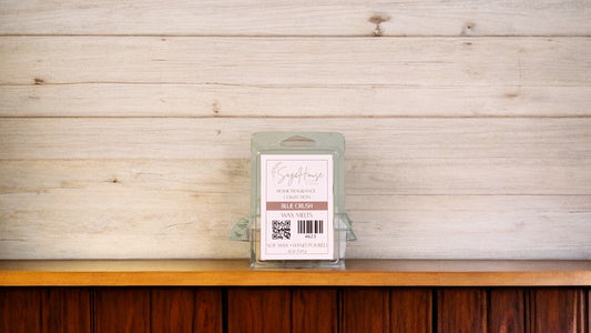 A clear clamshell container holding 6 wax melt cubes with a label on top, placed on a wooden surface against a wooden background.