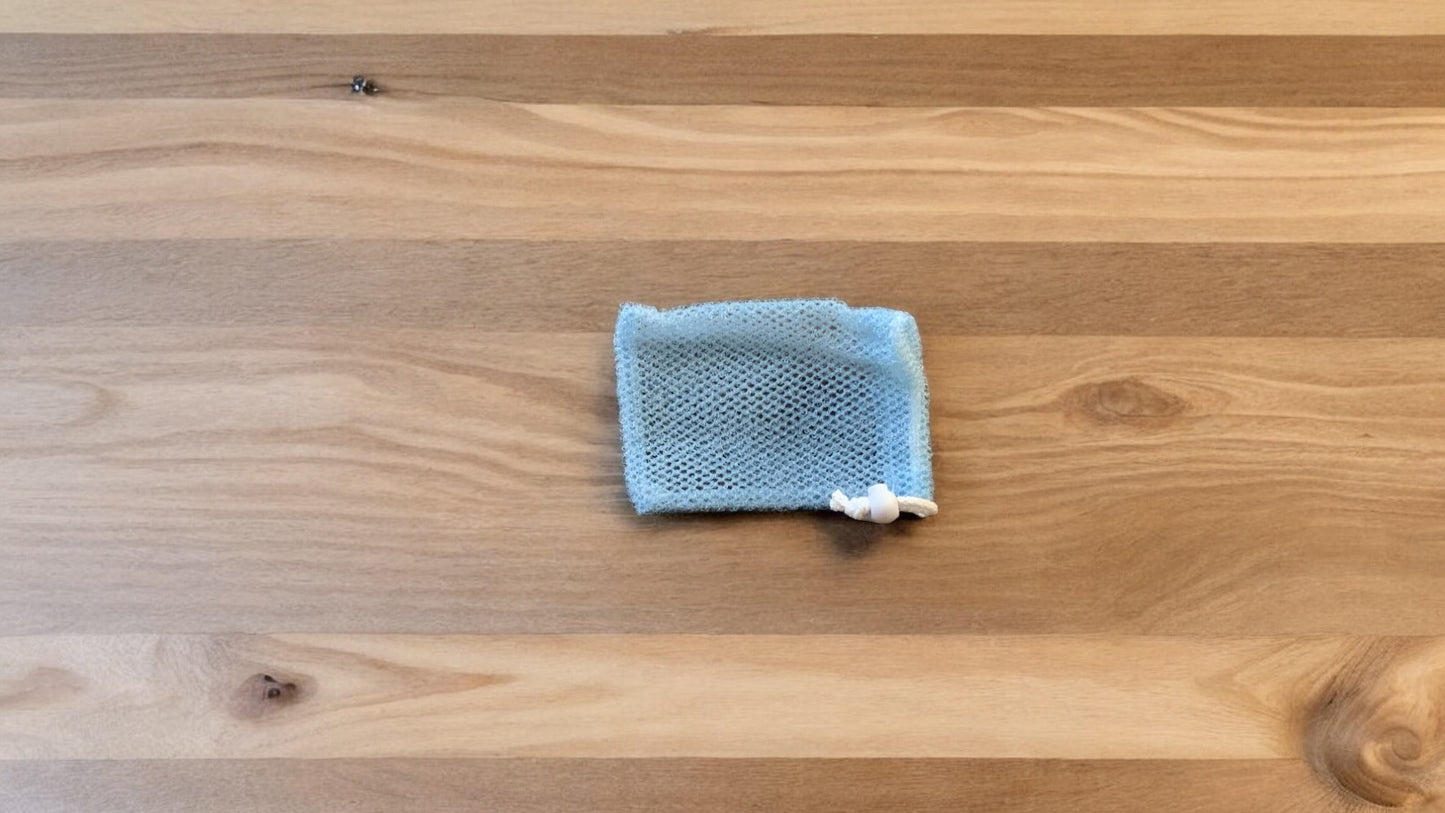 A Soap Scrub Pouch in blue, placed on a wooden surface.