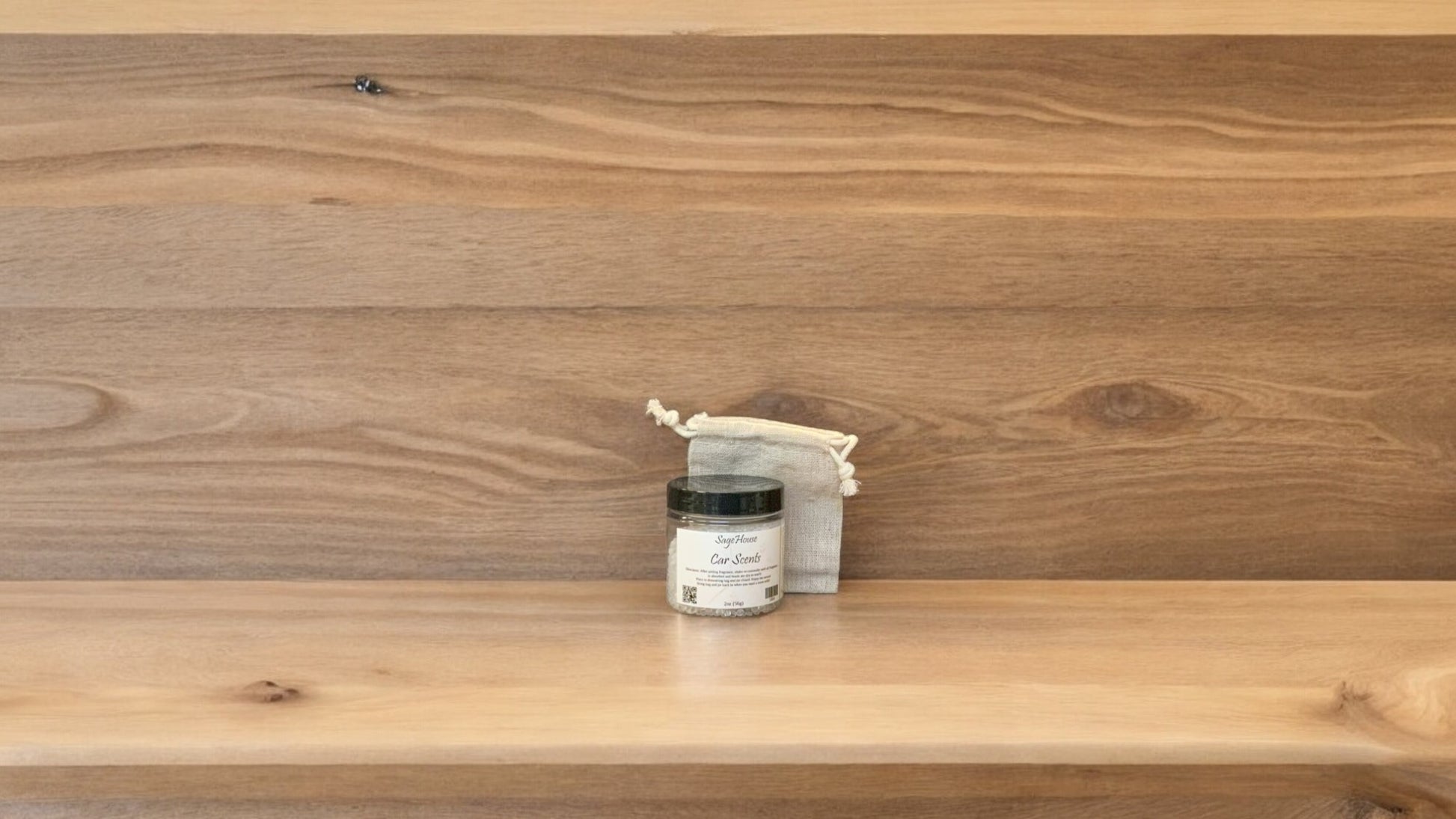 A small clear jar with a label and a sachet bag for car scent, placed on a wooden shelf.