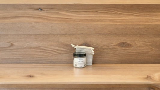 A small clear jar with a label and a sachet bag for car scent, placed on a wooden shelf.