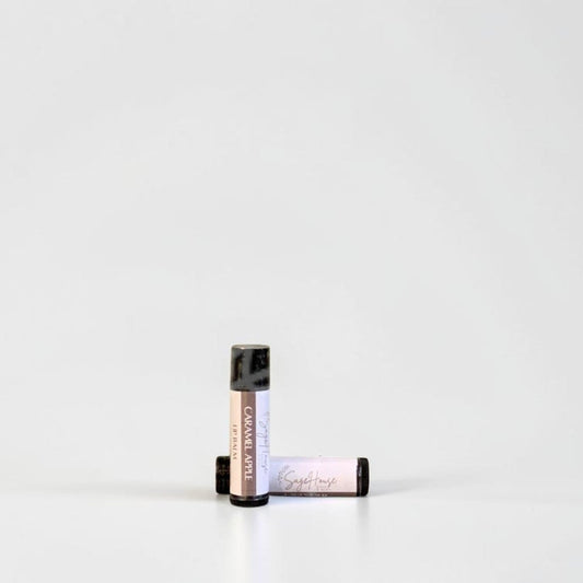 Two slim cylindrical lip balm tubes, one standing upright and one lying horizontally, positioned near the center of a clean white studio background.