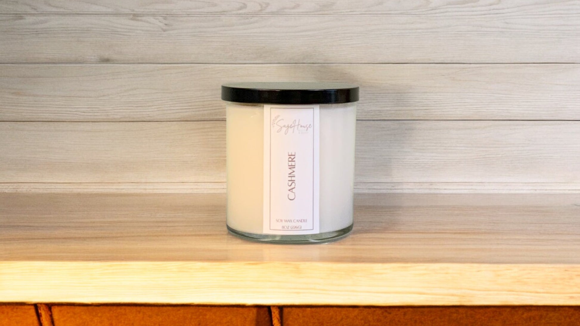 A white soy wax candle in a clear container, placed on a wooden surface, with a label on the front.