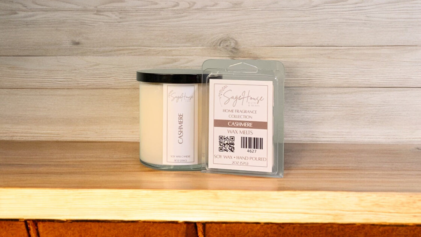A white soy wax candle in a clear container, next to a clear clamshell wax melt package. placed on a wooden surface, with a label on the front.