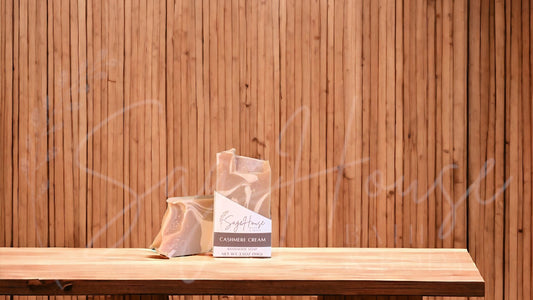 A tan bar of soap with white accents in a white labeled box, on a wood surface.