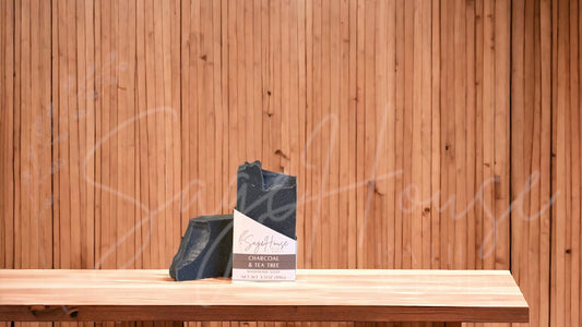A black bar of soap in a white labeled box, on a wood surface.