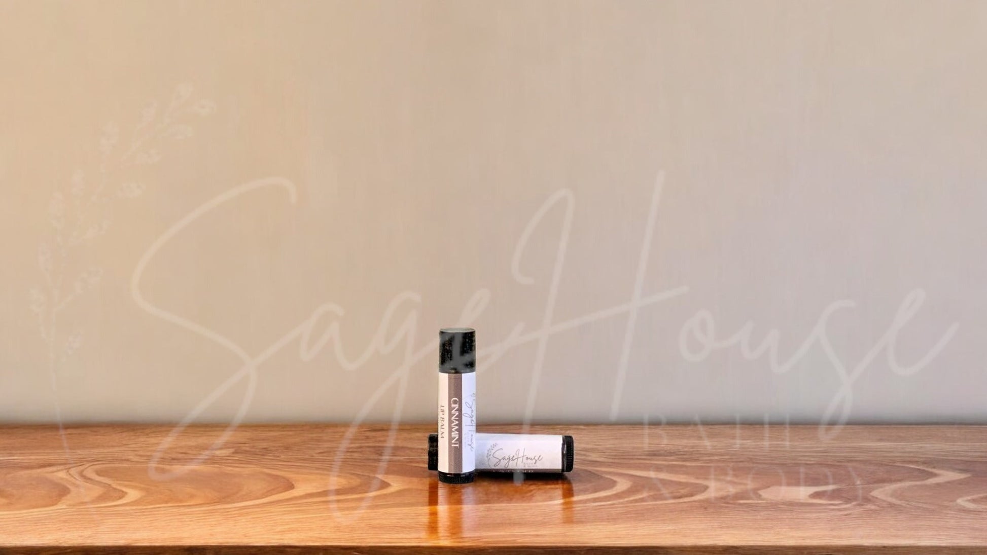 A tube of cinnamint lip balm placed upright with a tube lying behind it, on a wooden surface.