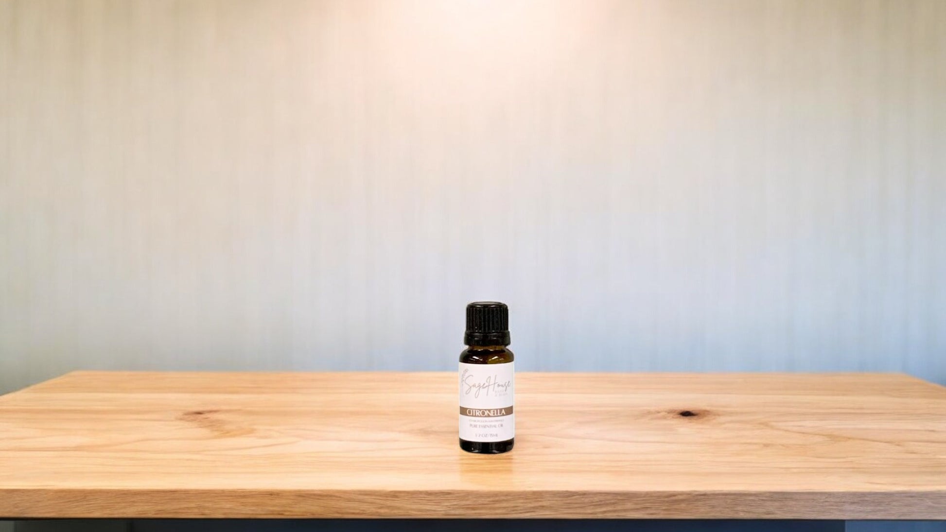 A small bottle of citronella essential oil is placed on a wooden surface with a plain background.