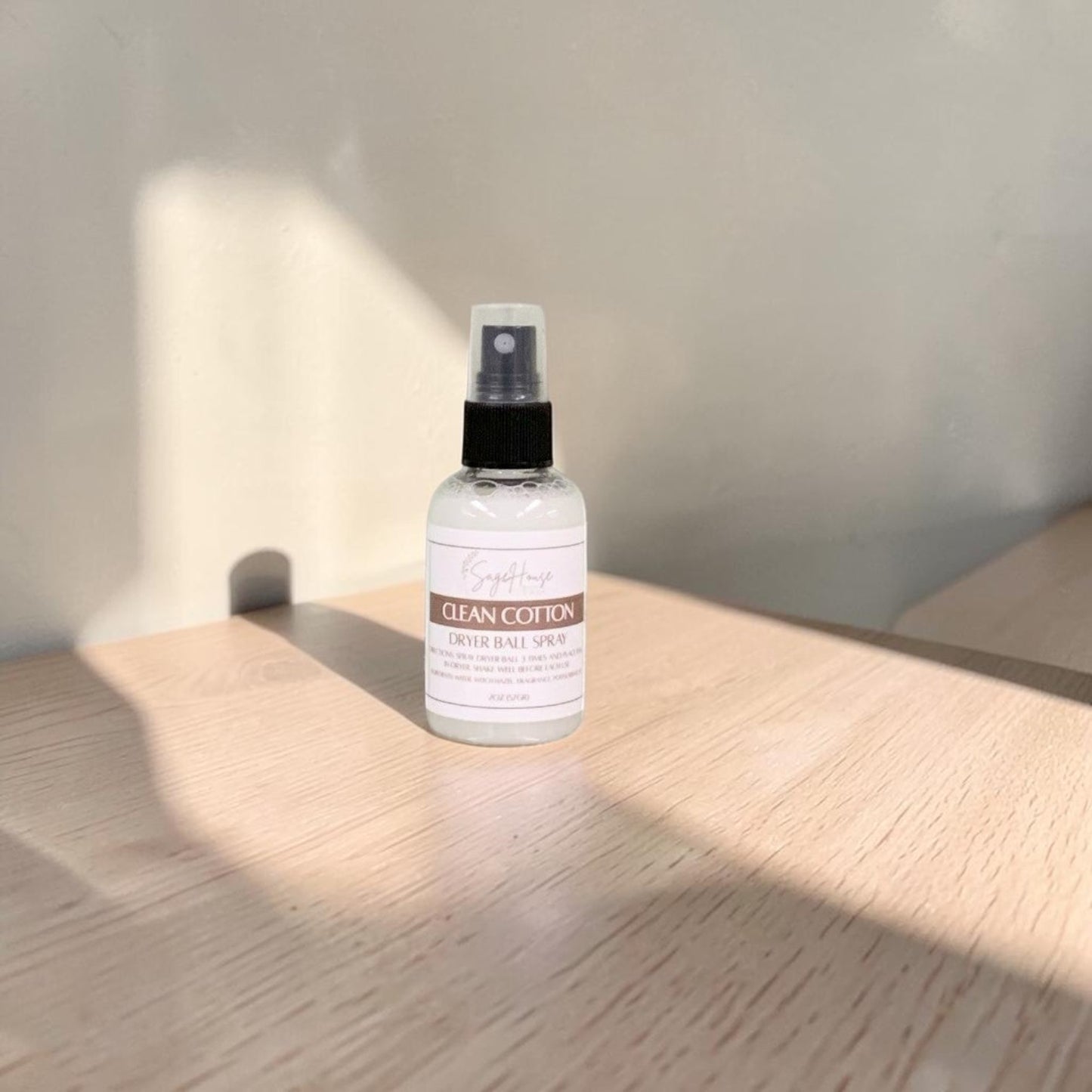 A clear bottle with black spritz top. sitting on a stone table with a white wall in the background