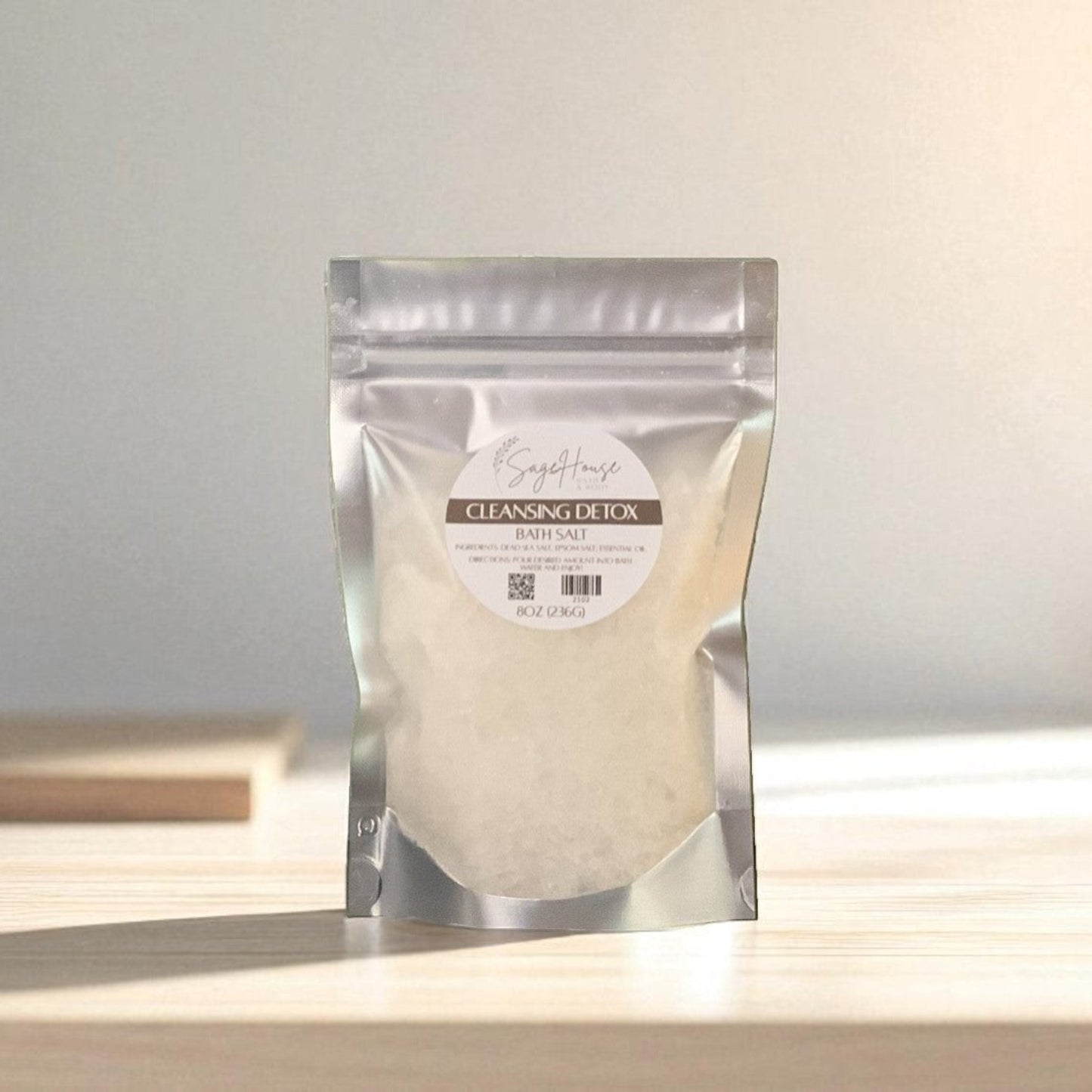 Silver packaging with a clear window of white salt labeled "cleansing detox" on a wood surface.
