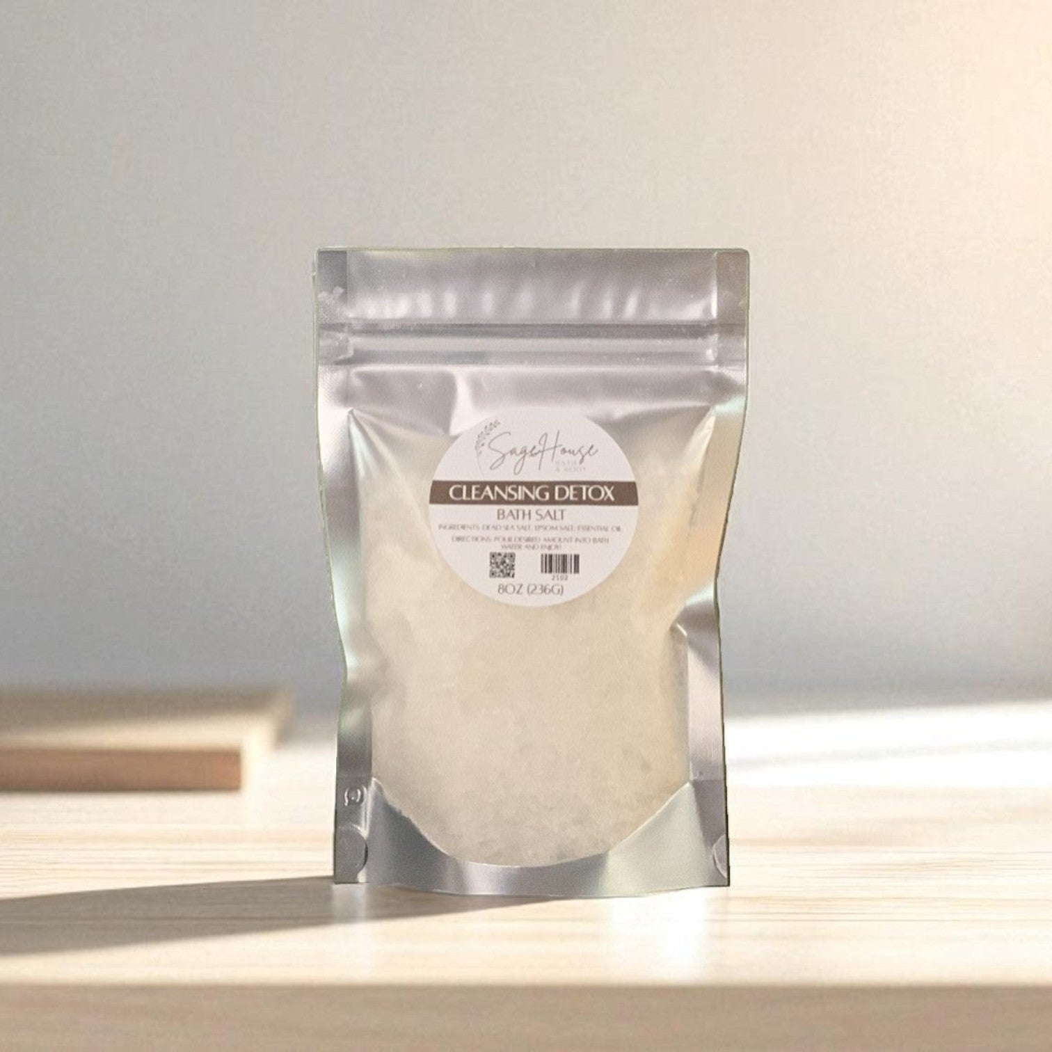 Silver packaging with a clear window of white salt labeled "cleansing detox" on a wood surface.