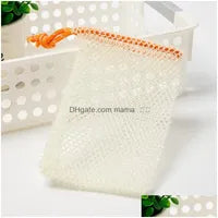 A Soap Scrub Pouch in cream, placed on a white surface. A basket and plant in the background.