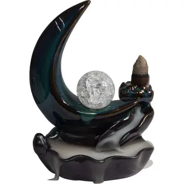 A cone incense burner shaped like the moon with a crystal ball in the center, with a waterfall of smoke going down into the attached bowl. On a white background.