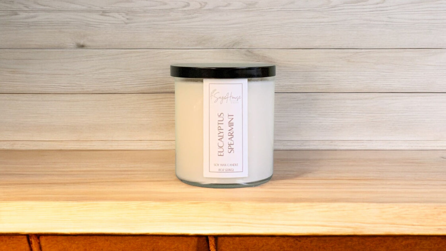A white soy wax candle in a clear container, placed on a wooden surface, with a label on the front.