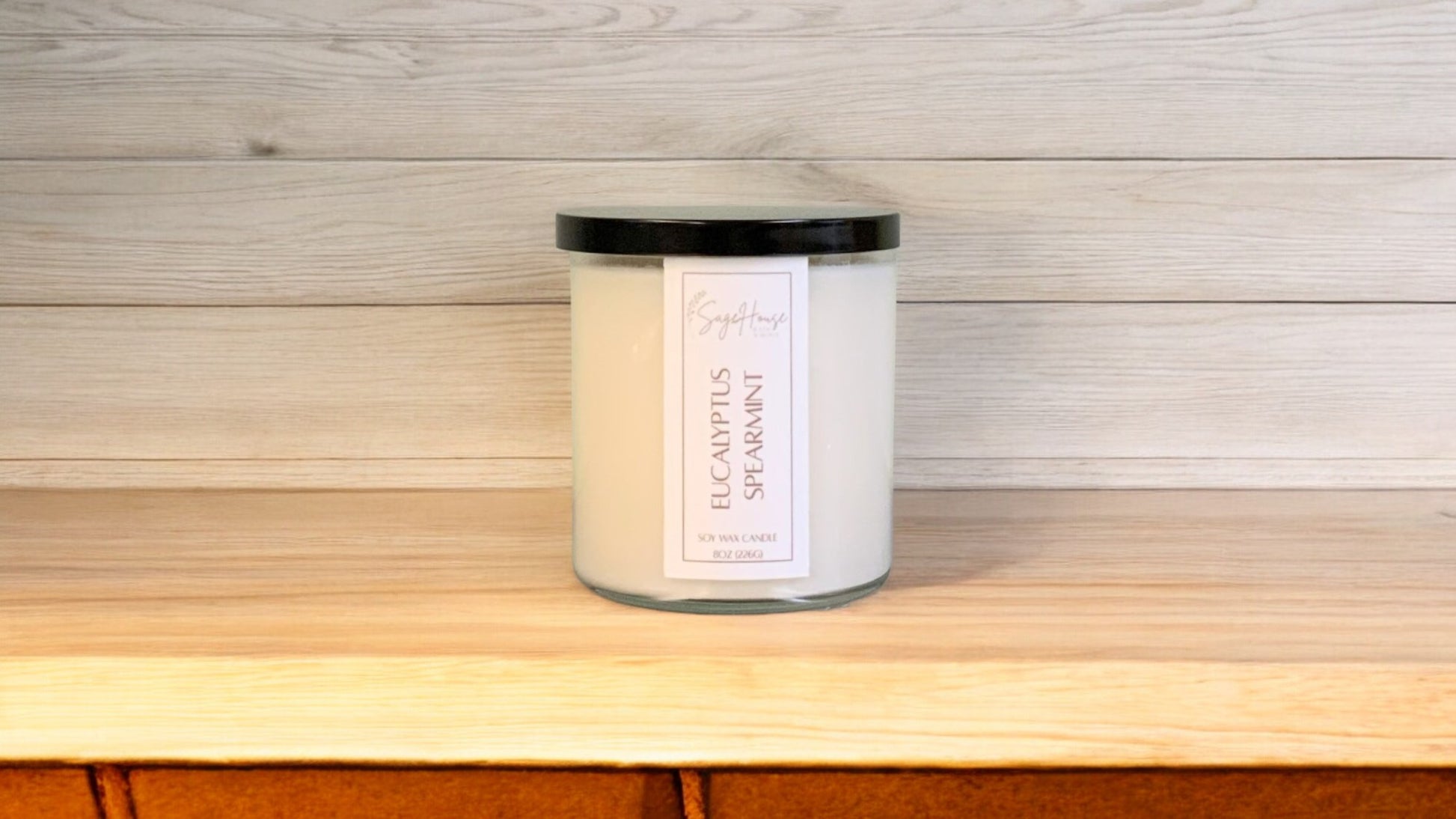 A white soy wax candle in a clear container, placed on a wooden surface, with a label on the front.