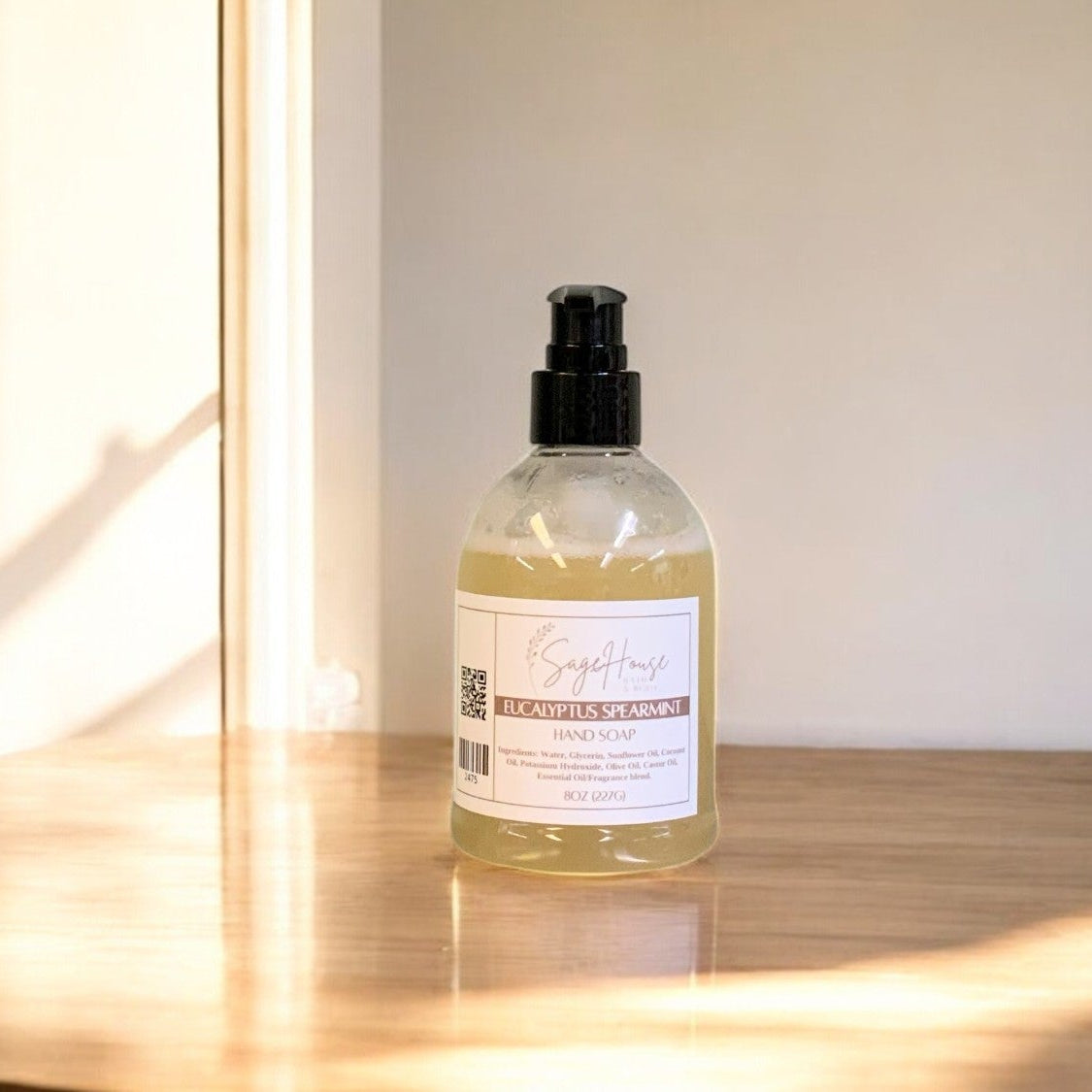 A clear plastic bottle of hand soap with a black cap, placed on a wooden surface with natural lighting.