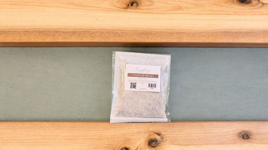 A large bath tea bag inside of a package. Sitting on a wood surface against a sage green background
