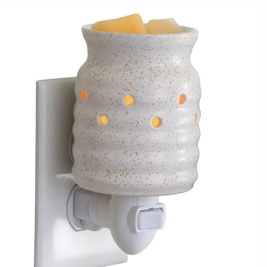 A ceramic wax warmer plug-in night light with a speckled off-white body, gold flecks, and glowing orange light holes, shown mounted on a white wall socket with wax melts inside.