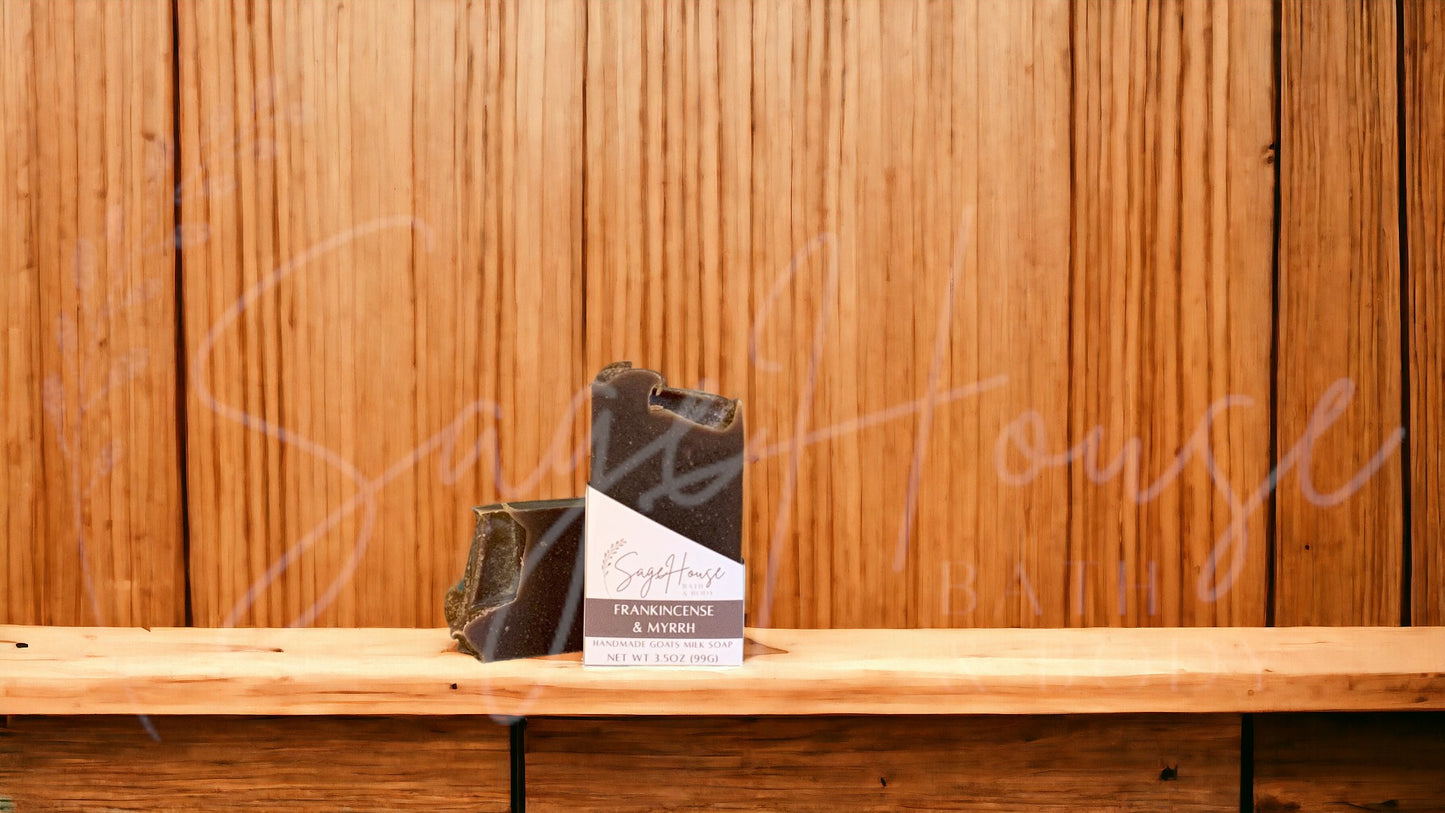 A dark brown bar of soap in a white labeled box, on a wood surface.