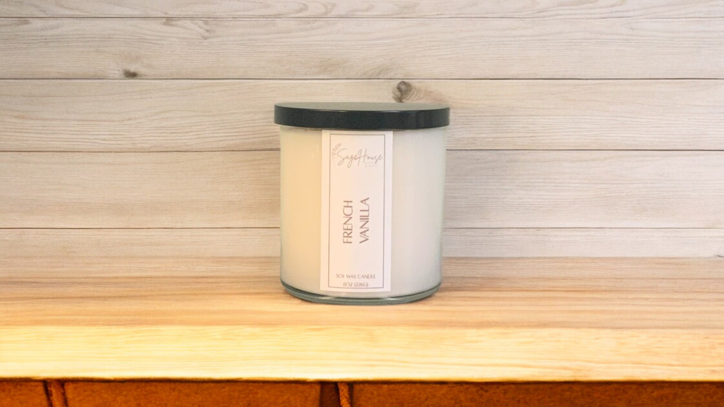 A white soy wax candle in a clear container, placed on a wooden surface, with a label on the front.