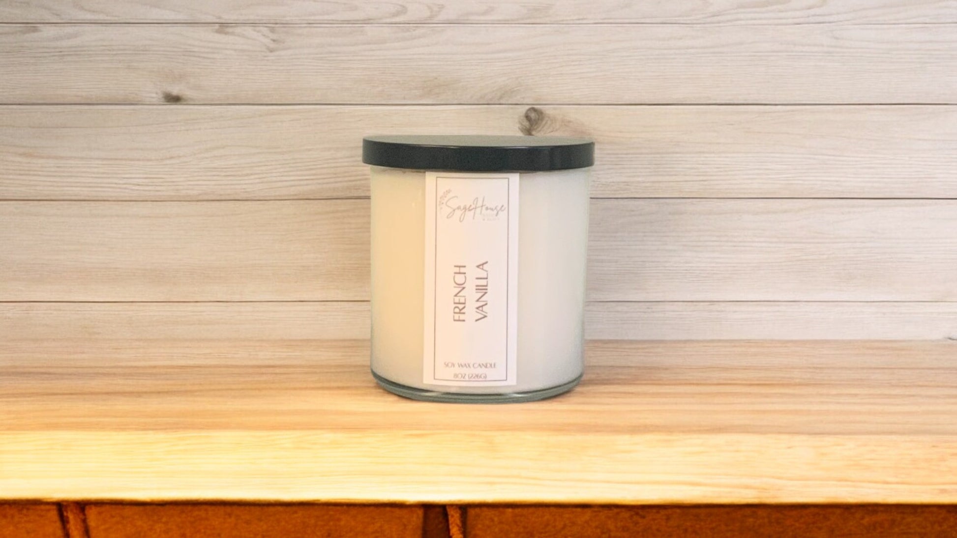 A white soy wax candle in a clear container, placed on a wooden surface, with a label on the front.