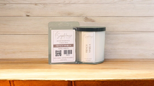A white soy wax candle in a clear container, next to a clear clamshell wax melt package. placed on a wooden surface, with a label on the front.
