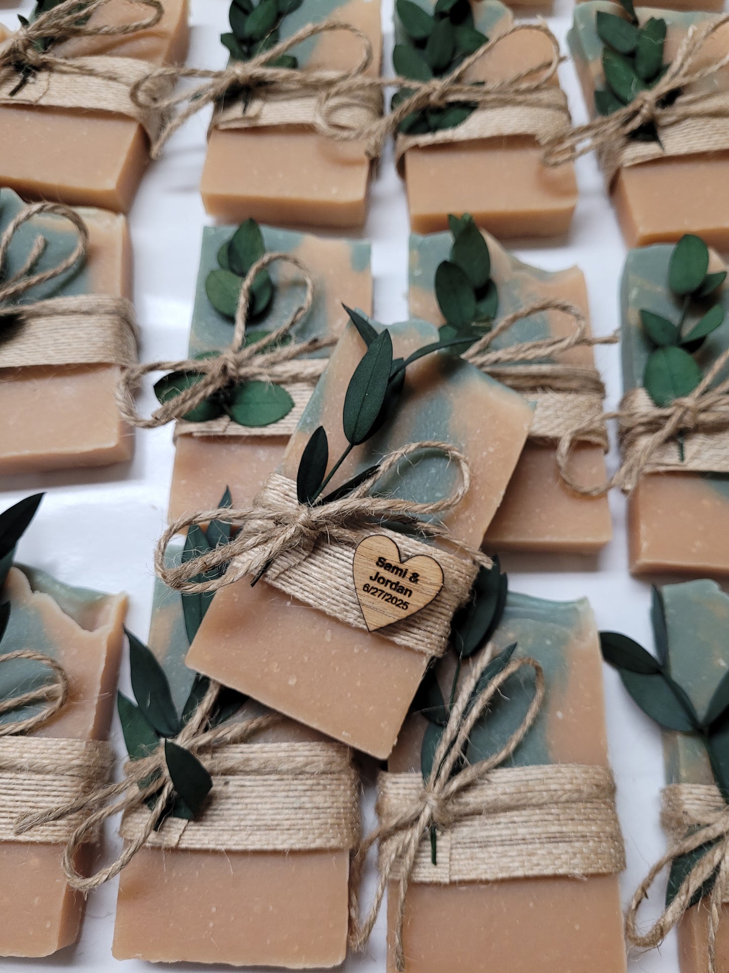 Handmade soap bars wrapped in brown twine with string and green leaves on a white background