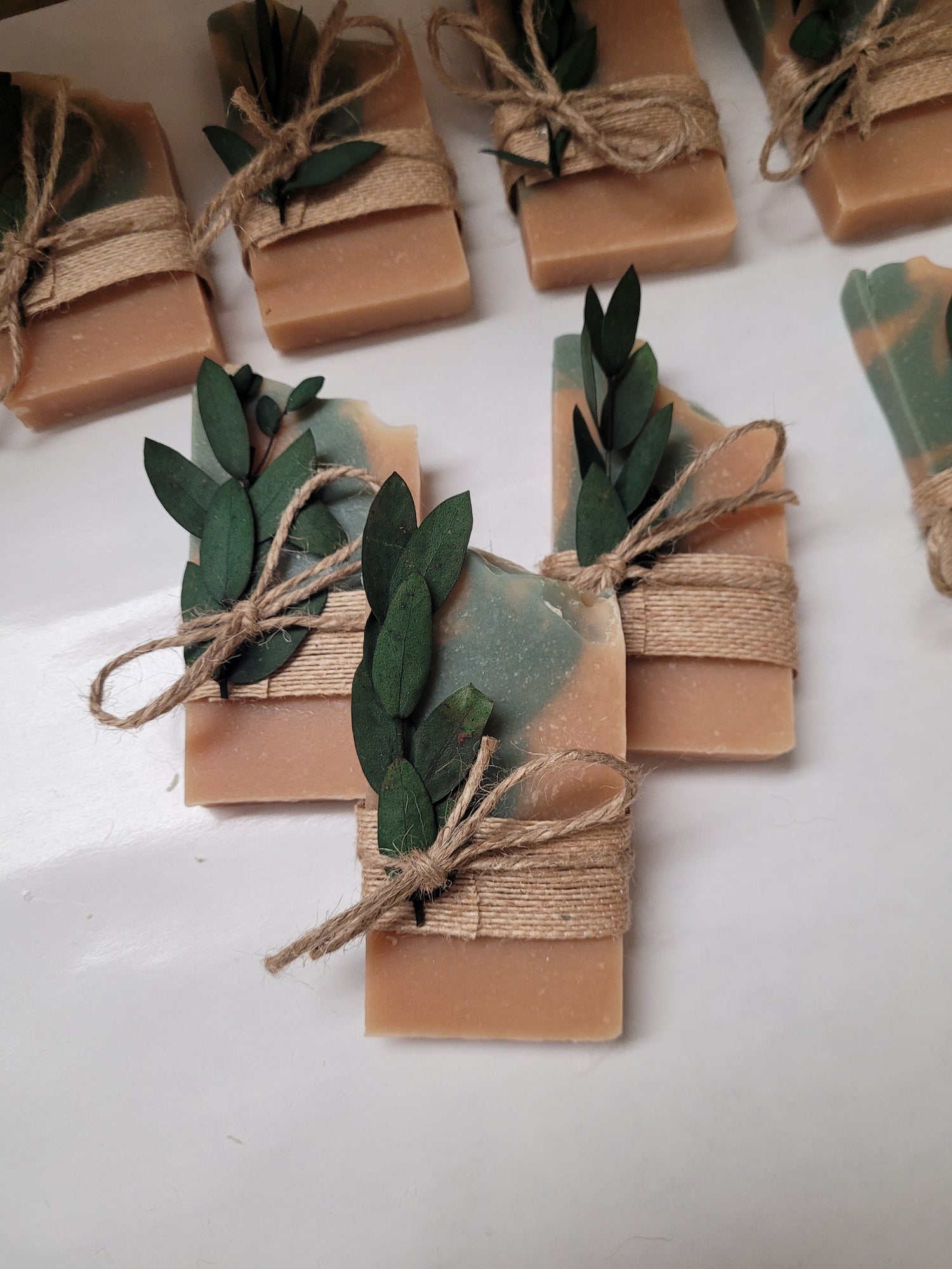 Handmade soap bars wrapped in brown twine with string and green leaves on a white background