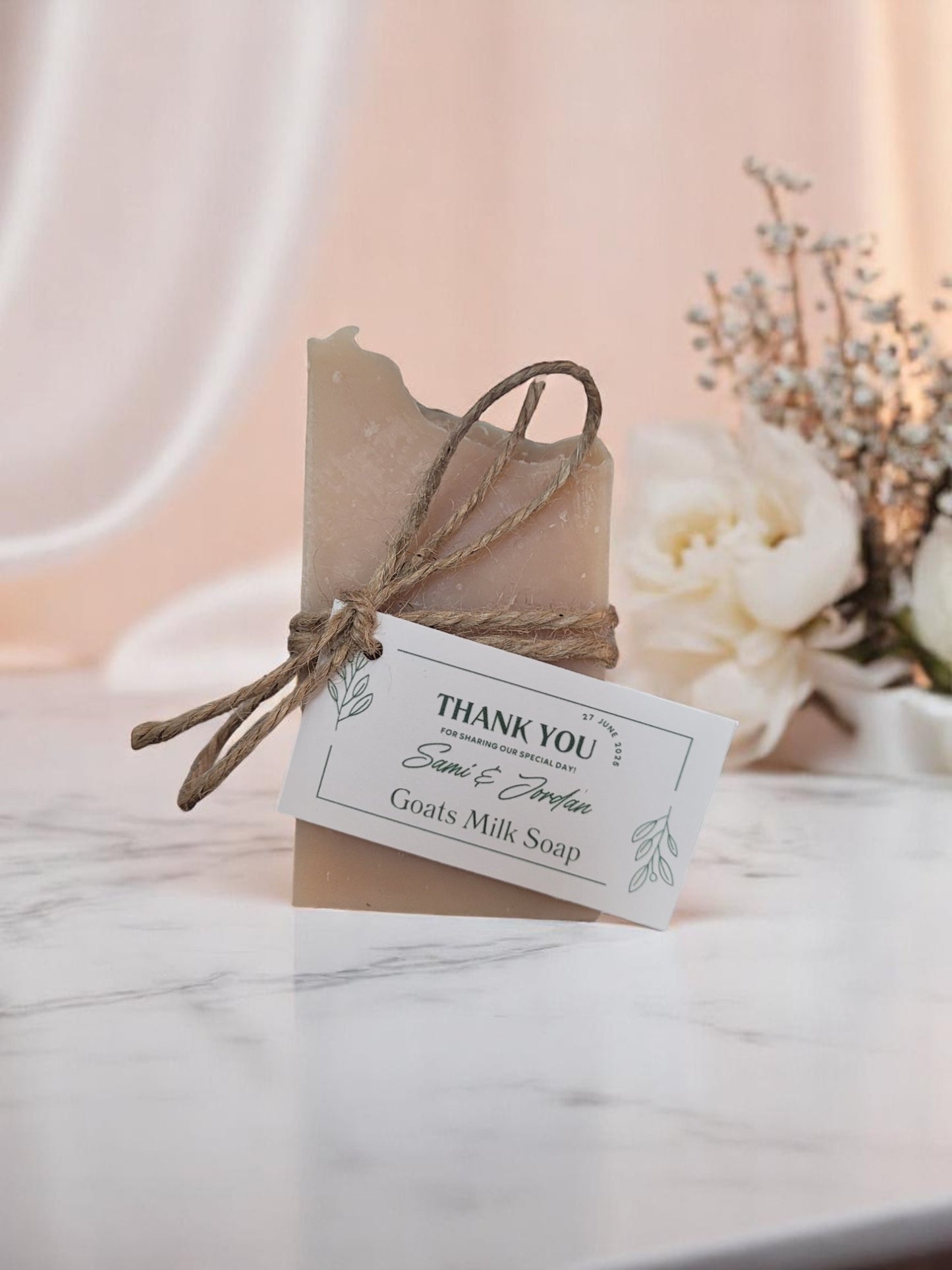 Goats milk soap wrapped in brown paper with a 'Thank You' tag on a marble surface.
