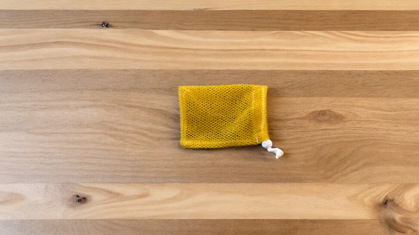 A Soap Scrub Pouch in gold, placed on a wooden surface.