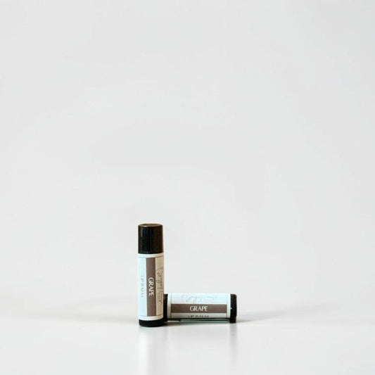 Two slim cylindrical lip balm tubes, one standing upright and one lying horizontally, positioned near the center of a clean white studio background.