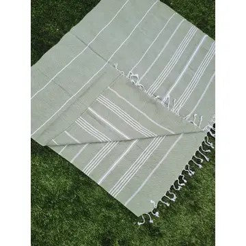 Green Turkish cotton towel, folded onto itself, on grass, on a white background.