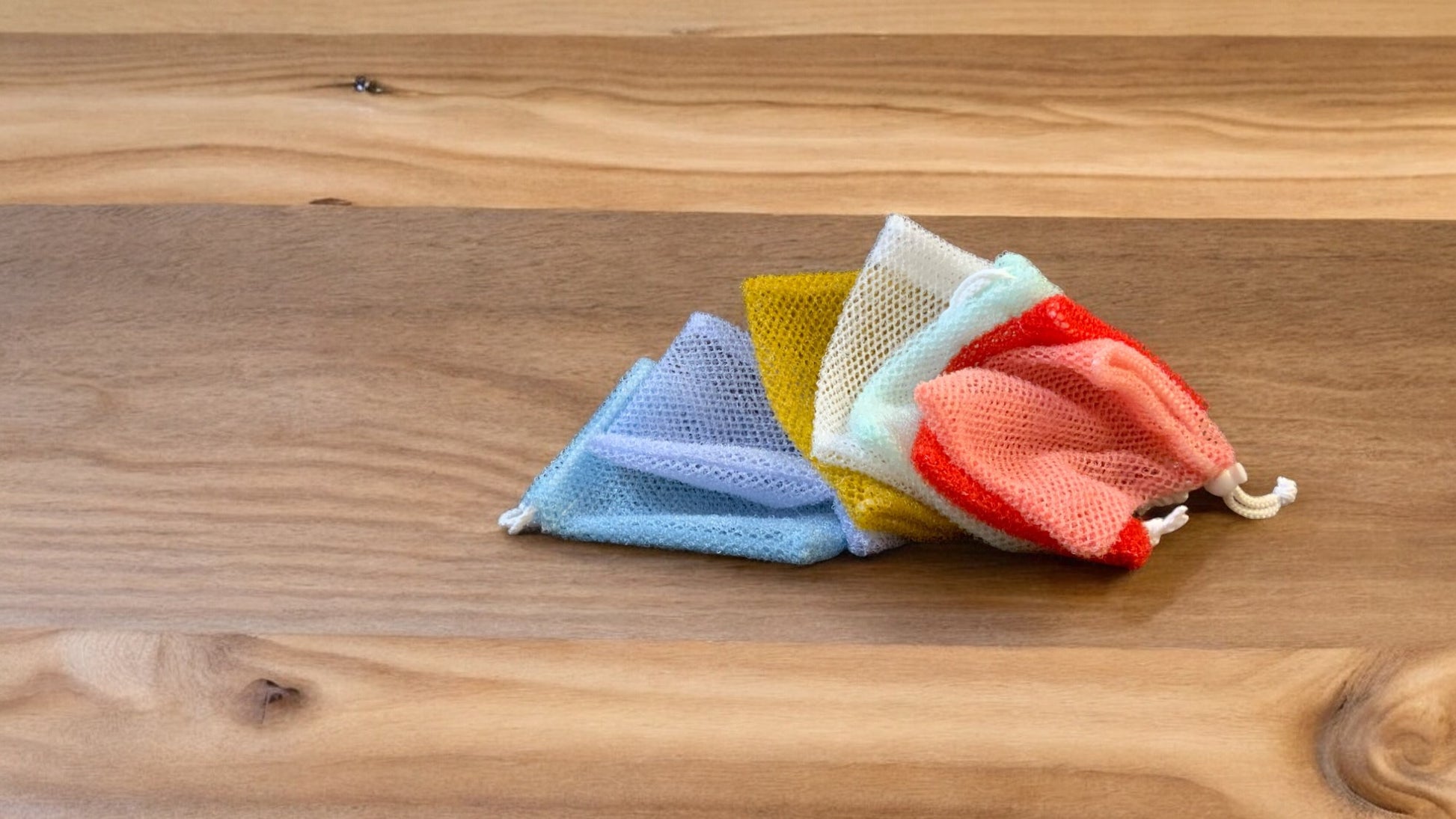 A group of Soap Scrub Pouches in various colors placed on a wooden surface.