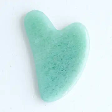 Heart-shaped green jade gua sha tool on a white background