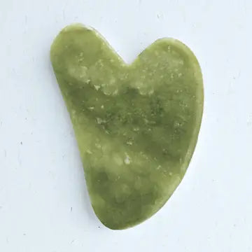 Green gua sha stone with a heart shape on a white background