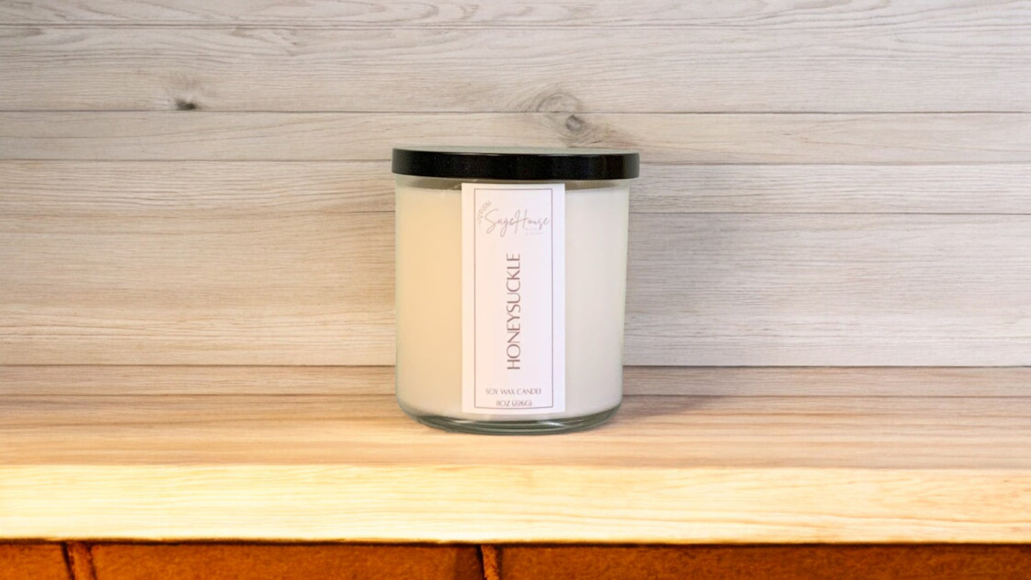A white soy wax candle in a clear container, placed on a wooden surface, with a label on the front.