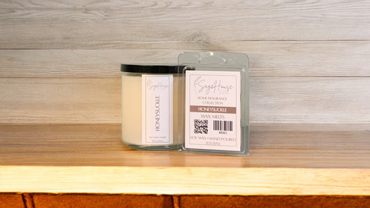 A white soy wax candle in a clear container, next to a clear clamshell wax melt package. placed on a wooden surface, with a label on the front.