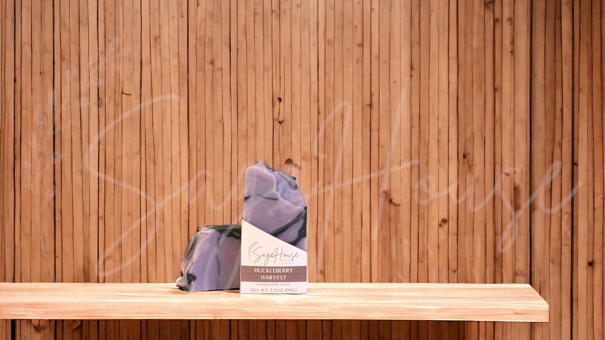 A purple colored bar of soap with black accents in a white labeled box, on a wood surface.