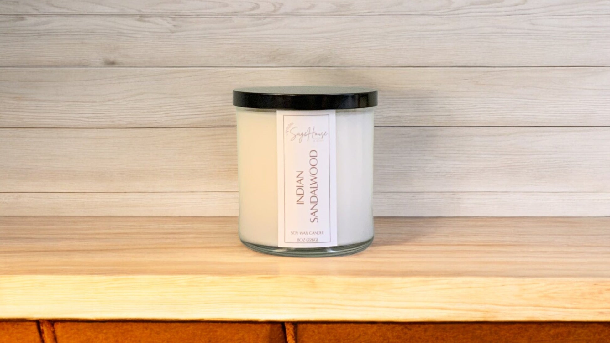 A white soy wax candle in a clear container, placed on a wooden surface, with a label on the front.