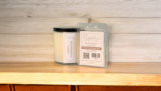 A white soy wax candle in a clear container, next to a clear clamshell wax melt package. placed on a wooden surface, with a label on the front.