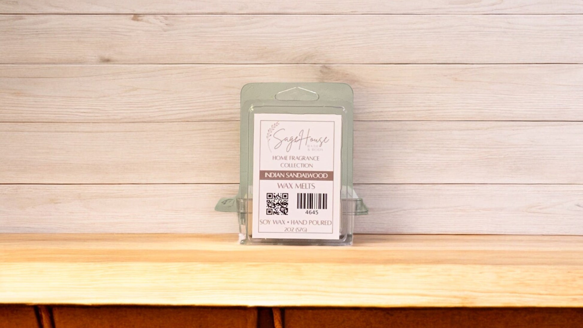 A clear clamshell container holding 6 wax melt cubes with a label on top, placed on a wooden surface against a wooden background.