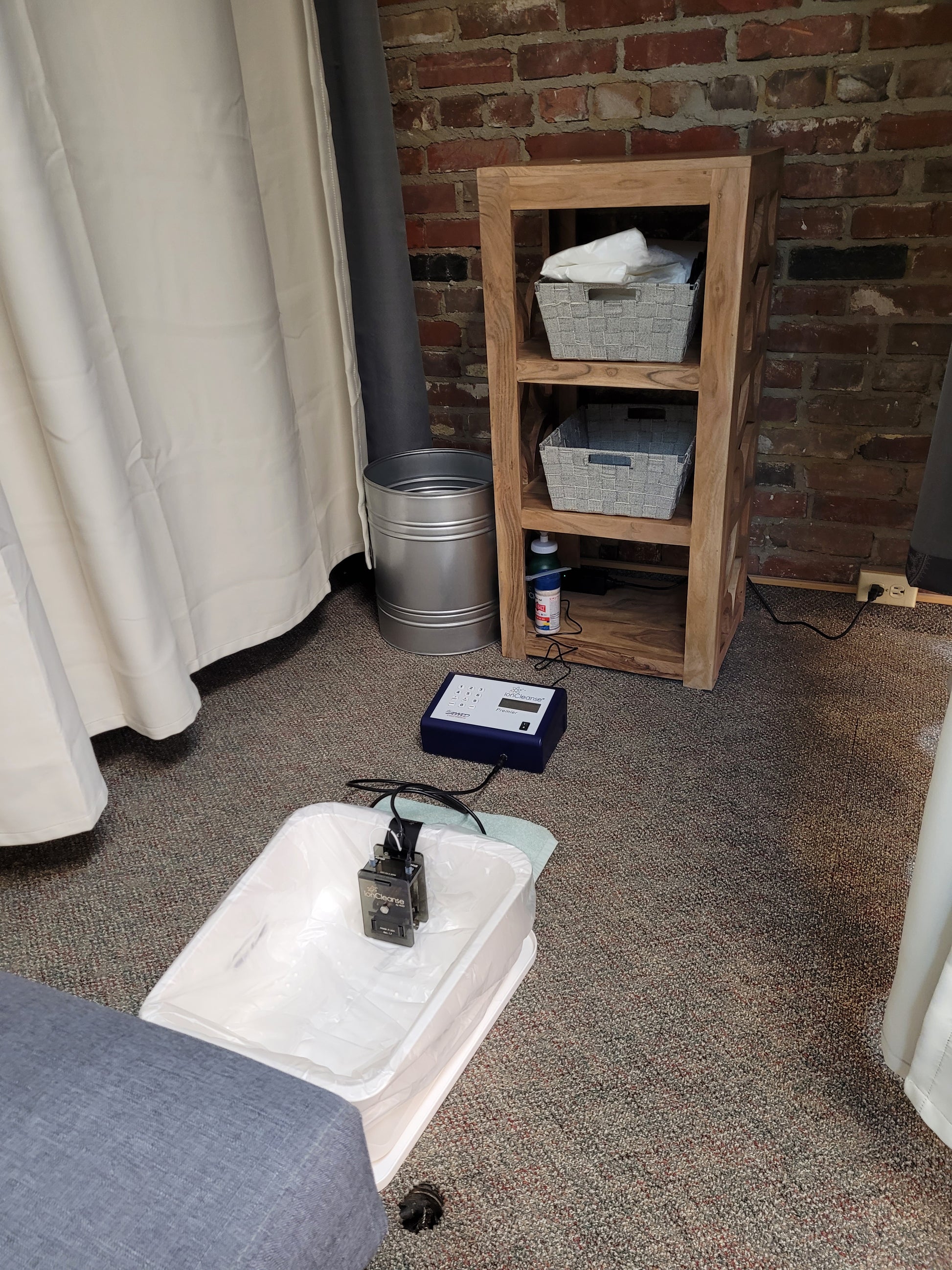 An Ionic foot cleanse machine set up with a white tub, with a wooden shelf in the background containing towels and personal items.