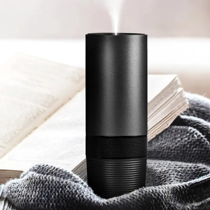 A black modern essential diffuser on a gray blanket with a book in the background