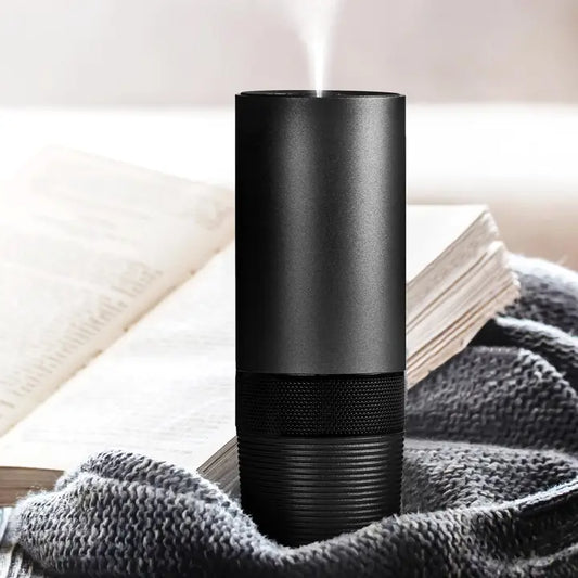 A black modern essential diffuser on a gray blanket with a book in the background