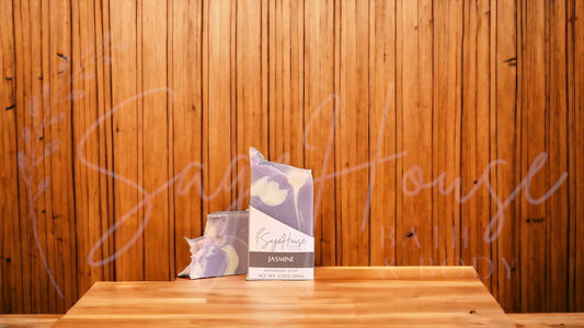 A purple colored bar of soap with white accents in a white labeled box, on a wood surface.