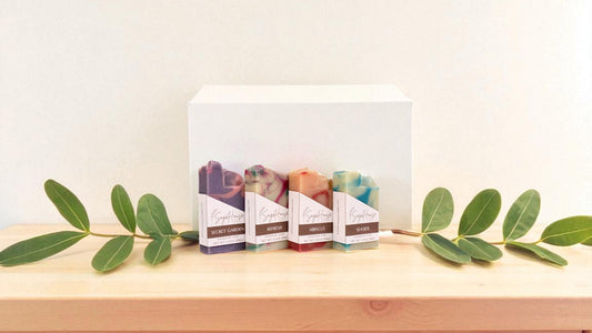 Set of soap bars with packaging on a wooden surface with green leaves