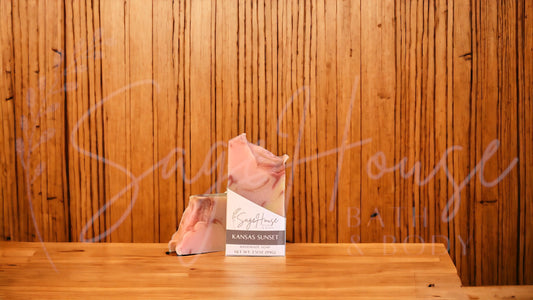 A peach colored bar of soap with yellow and red accents in a white labeled box, on a wood surface.