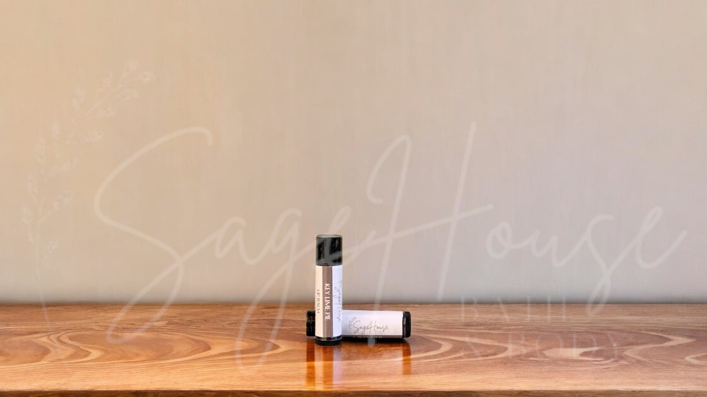 A tube of key lime pie lip balm placed upright with a tube lying behind it, on a wooden surface.