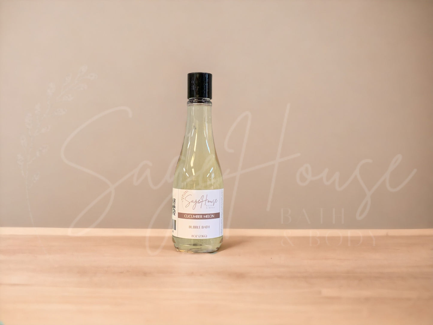 A bottle of Sage House bubble bath, labeled 'cucumber melon'. Placed on a wooden surface.