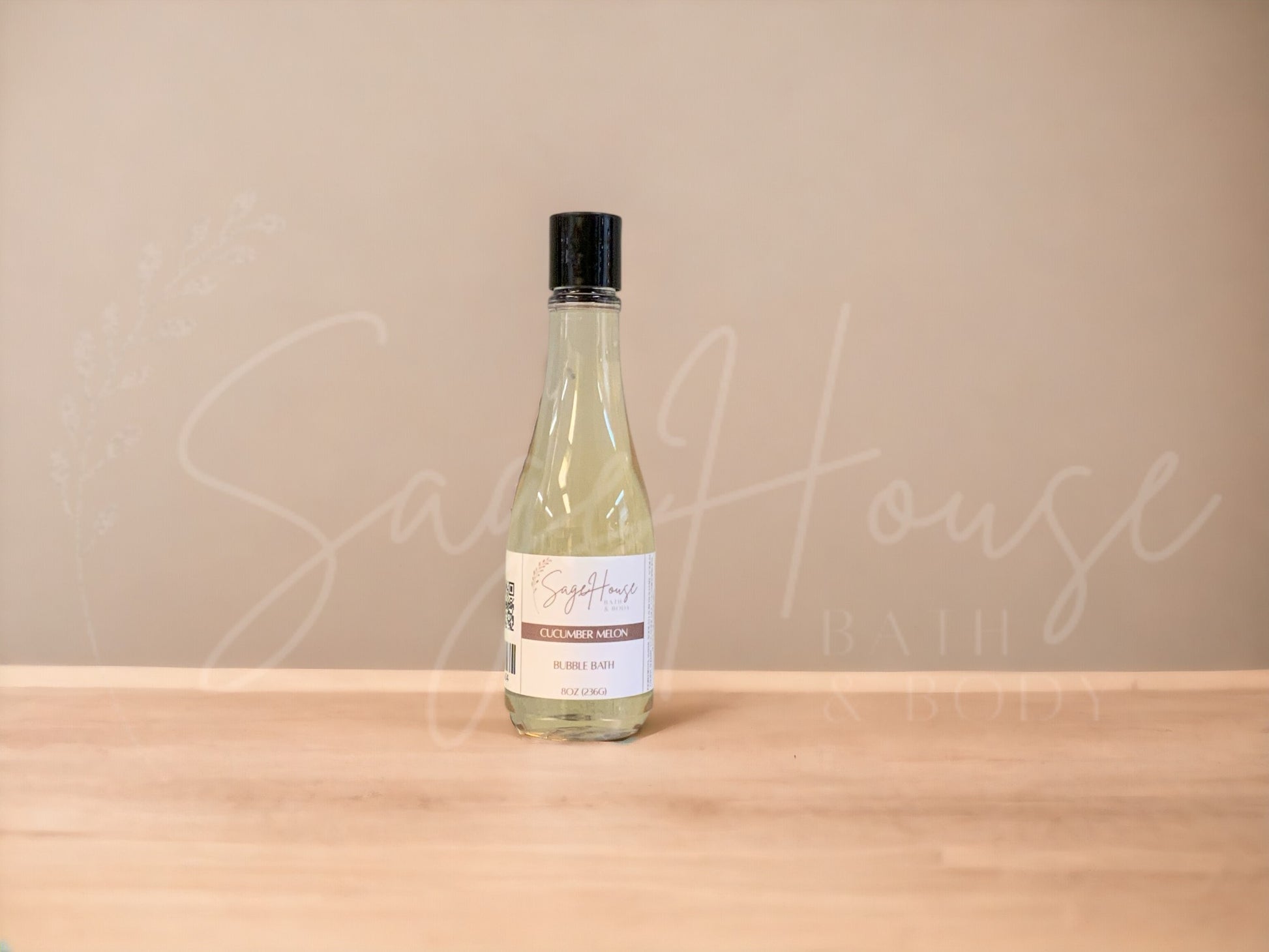 A bottle of Sage House bubble bath, labeled 'cucumber melon'. Placed on a wooden surface.